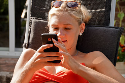 Close-up of young woman using mobile phone while sitting on chair in yard
