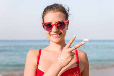 Portrait of woman wearing sunglasses with lotion standing against sea