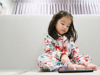 Cute asian girl sitting and playing game on mobile phone at home