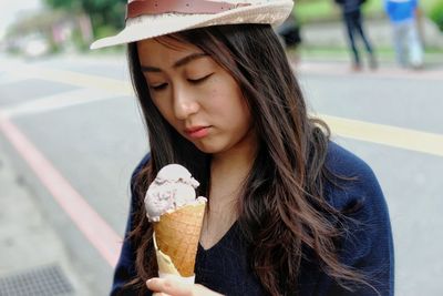 Close-up of young woman having ice cream cone while standing on street