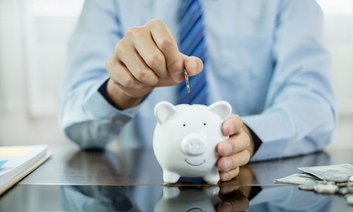 Midsection of businessman putting coin in piggy bank