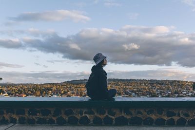 Woman sitting on wall against sky