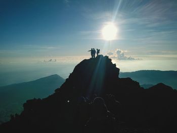 Silhouette friends standing on cliff during sunny day