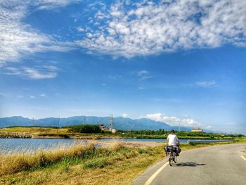 Rear view of man riding bicycle on road against blue sky