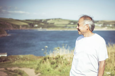 Senior man looking away while standing on field by lake