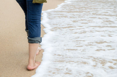 Low section of man standing on sand at beach