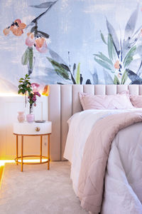 Interior of bedroom with floral ornament on wall with comfortable bed under blanket placed near round bedside table with vase of fresh plants