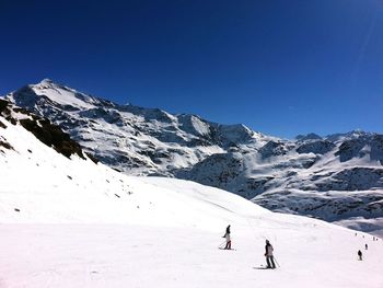 People skiing on snow covered landscape against clear sky