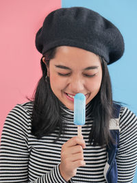 Close-up of smiling young woman holding popsicle stick against wall