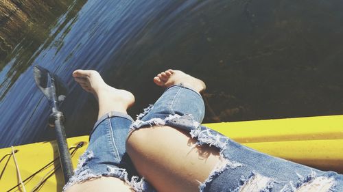 Low section of woman wearing torn jeans sitting on boat in lake