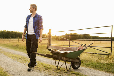 Farmer walking by wheelbarrow on grassy field during sunny day