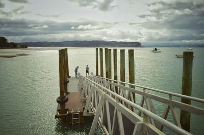 Men on pier over lake against cloudy sky