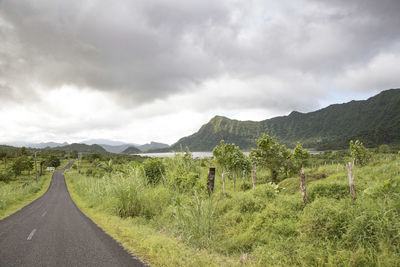 Empty road next to lake and exotic green mountains during cloudy day