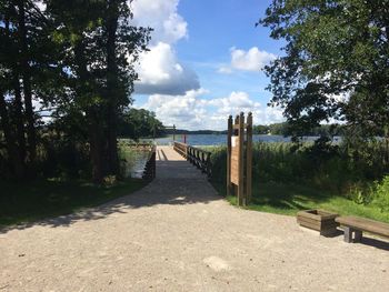 Walkway by trees against sky