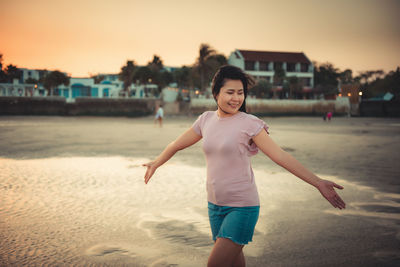 Smiling young woman walking at beach during sunset