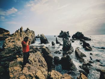 Rear view of woman standing on rock by sea