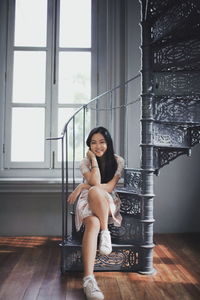 Portrait of smiling young woman sitting on spiral staircase at home