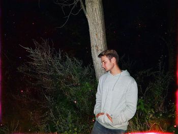 Young man looking away while standing on tree