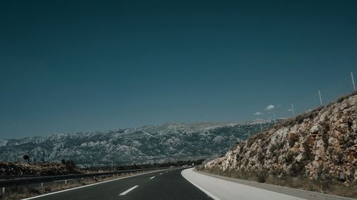 Road leading towards mountains against clear sky