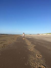 Man walking on beach against clear blue sky