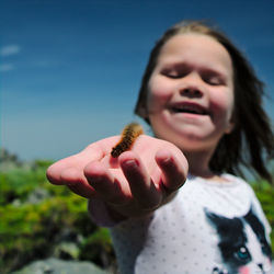 Cute girl holding caterpillar against sky