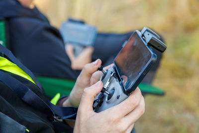 Drone operator hands using remote control with sticks and cellphone as monitor at daylight