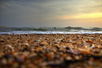 Pebbles on beach against sky during sunset