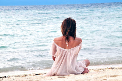 Rear view of woman sitting on shore at beach