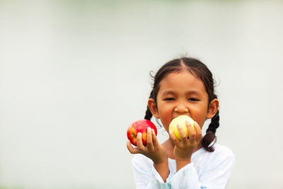 Portrait of cute girl holding apple against white background