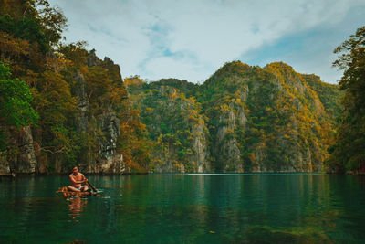 Man on wooden raft in lake against mountain