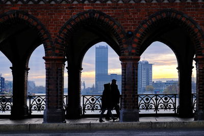 Rear view of silhouette woman standing by buildings against sky