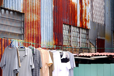 T-shirts and shirts hanging on clothesline against corrugated wall