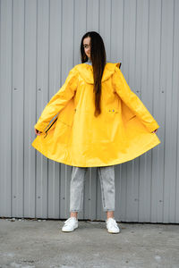 Girl in a yellow raincoat and gray jeans stands on a gray background. youth subculture