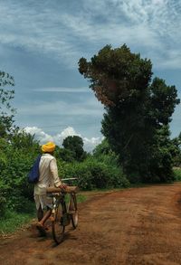 Rear view of man with bicycle walking on dirt road