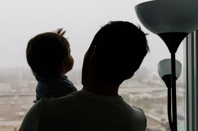 Rear view of young father and toddler against window