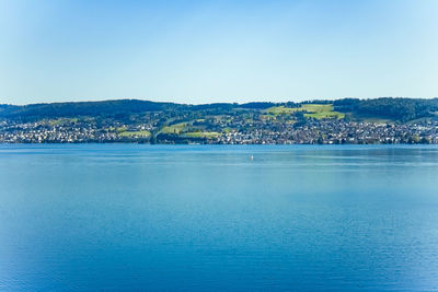 Scenic view of sea by city against clear blue sky