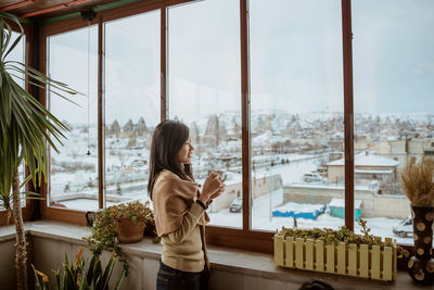 Side view of woman looking through window