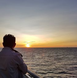 Rear view of mature man by railing against sea during sunset