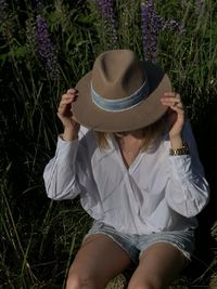 Midsection of woman wearing hat sitting on field