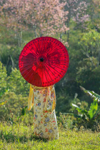 Woman with red umbrella standing on field