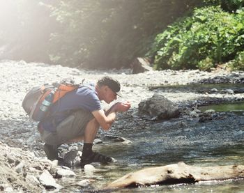 Side view of mature man drinking water from river in forest