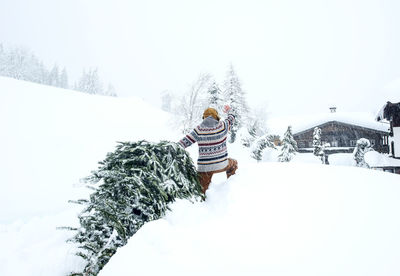 Man coming home, waving and pulling christmas tree in the snow