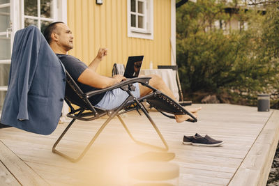 Thoughtful mature man with laptop sitting in patio of holiday villa