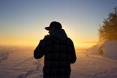 Rear view of man standing on snow covered land during sunset