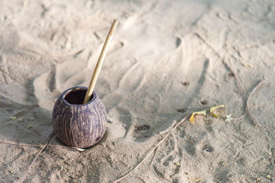 High angle view of coconut container with wooden straw on sandy beach