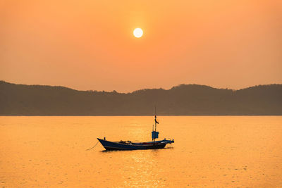 Silhouette sailboat on sea against orange sky