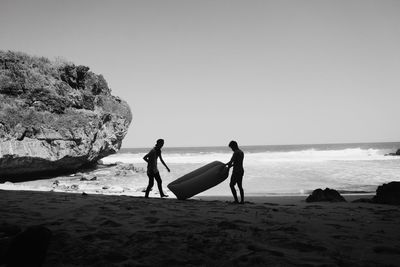 Man carrying inflatable tube while walking on beach