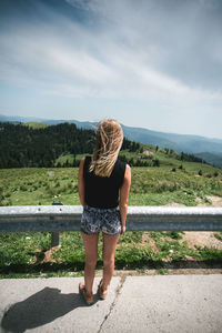 Rear view of young woman standing against sky