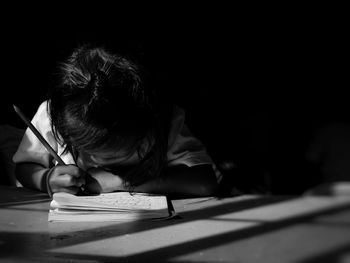 Girl writing homework on table while sitting in darkroom