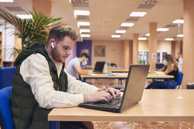 A young boy sitting and working with his laptop in the library